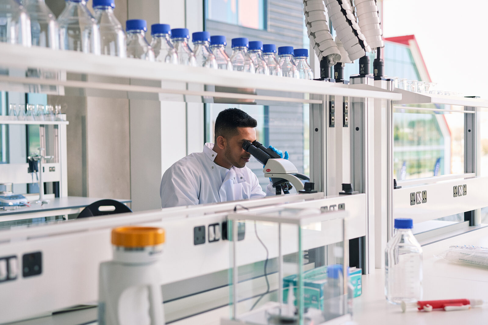 A scientist at a microscope on a lab bench